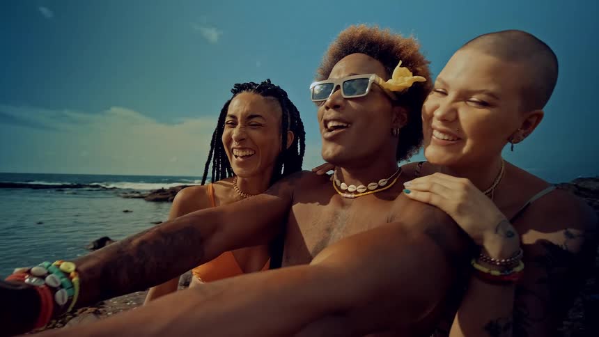 Three black people talking and laughing into a phone at a beach scene