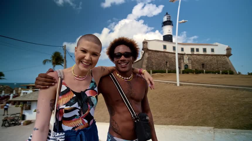 Man and a woman embraced together at a natural landmark with a beach in the background