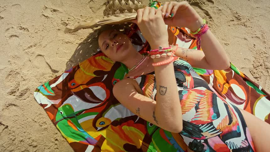 Woman holding a hat lying on a towel on the sand of a beach