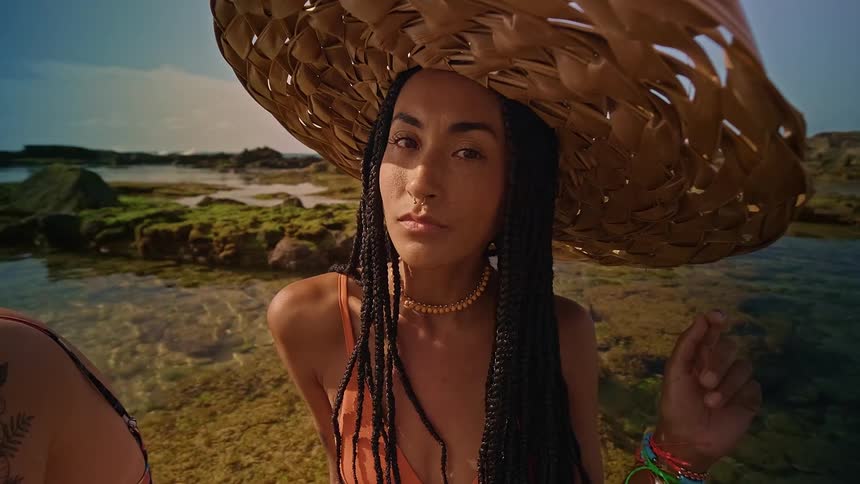 A woman wearing a beach hat posing while sitting in the sea at the beach
