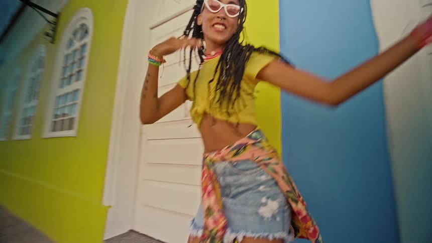 The video shows two young women smiling and dancing with each other one of the women has brown hair with blonde highlights and is wearing a yellow top with a pair of denim jeans the other woman has black hair with a braid and is wearing a white dress