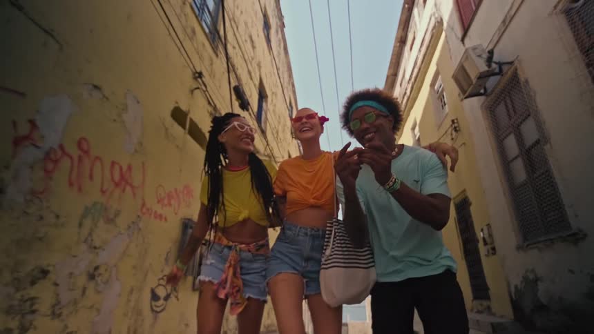 The video shows a lowangle shot of three young people walking down a narrow alleyway with yellow graffiticovered walls all three are smiling and appear to be enjoying themselves
