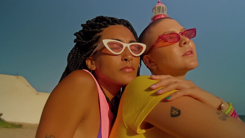 The provided video does not contain any text to describe it shows two women on a beach with a lighthouse in the background there is a watermark that reads filmsupply across the video