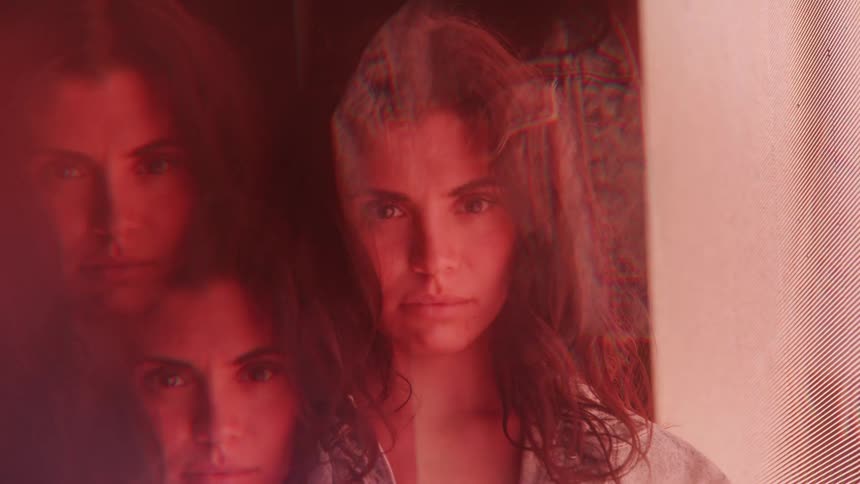 A video clip with a psychedelic kaleidoscopic effect shows a woman with long brown hair the womans face is seen multiple times on the left side of the frame with her eyes closed while her full face is visible in the center with her eyes open