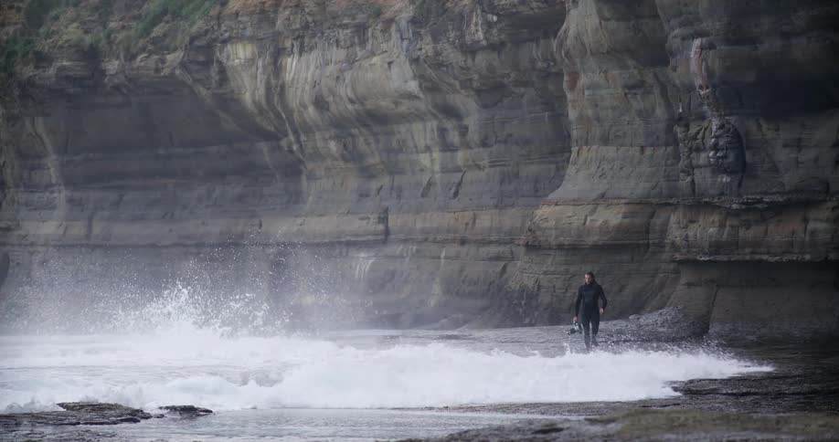 Huge wave crashes against the rocks as a person walks near the cliff