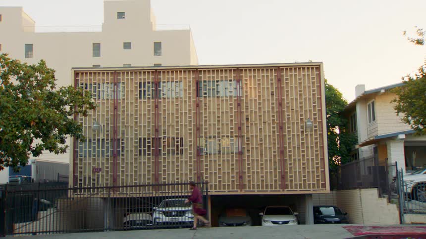 Man walking in front of a building with a decorative block facade and an open garage with parked cars