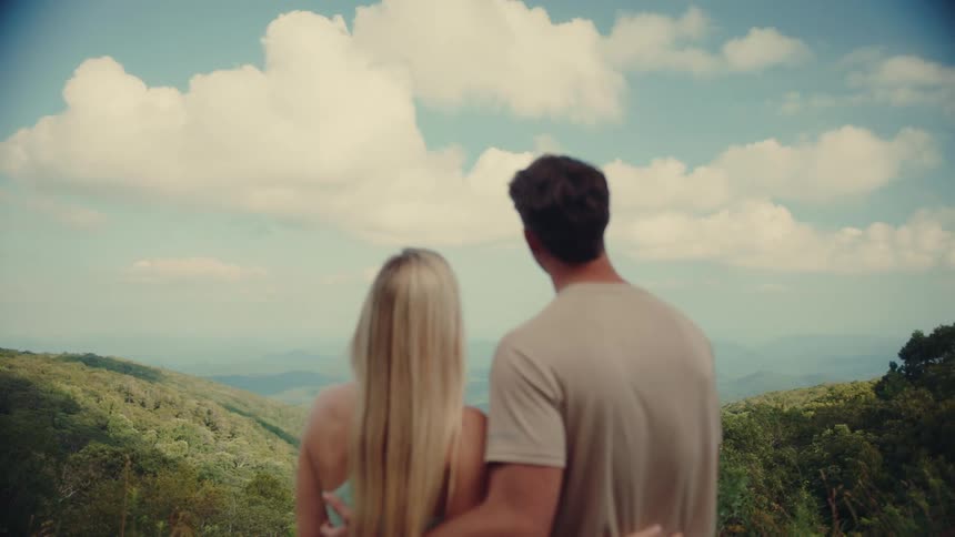 Couple stands on a mountain overlooking a scenic landscape