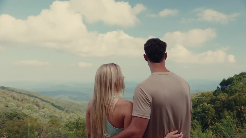 Man kissing his girlfriend on the forehead while they are outdoors with a view of mountains