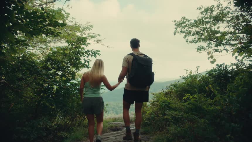 A couple holding hands while hiking to a forest viewpoint