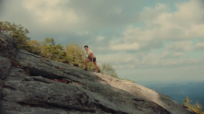 A couple climbing up a steep rocky hill on a cloudy summer day