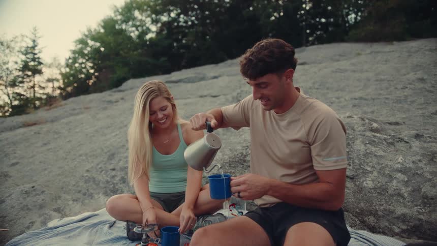 Man and woman sitting on a rock in the mountain and serving tea