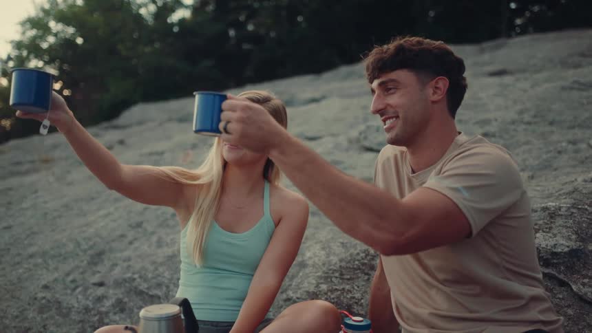 Couple toasting blue cups while sitting on a rock