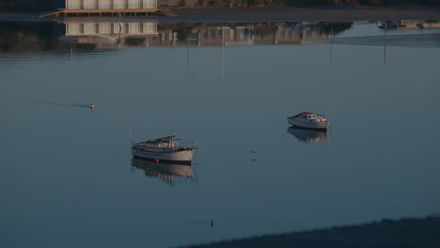 Two boats still on calm waters with building reflections