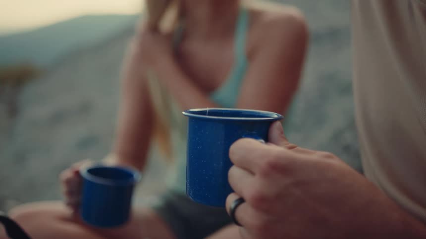 Two people holding blue mugs while chatting outdoors