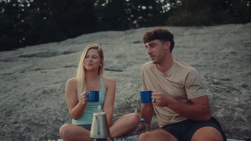 Couple sitting on a rock in the mountain drinking tea from blue cups