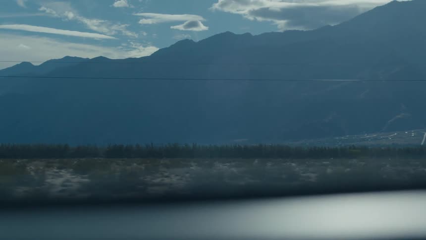 The video shows a darkcolored car driving past the camera with a mountain range in the background the car is sleek and modern and it appears to be moving at a fast pace the mountains are large and jagged and they are covered in a light dusting of sno