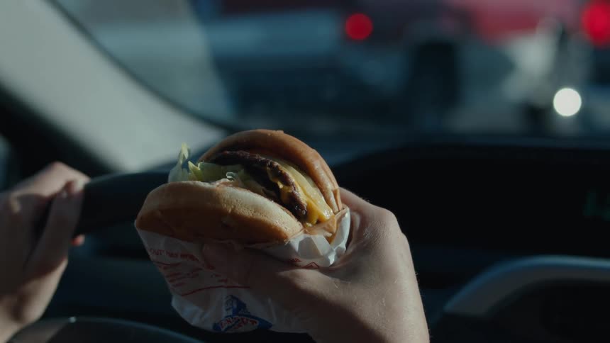 Person driving a car and holding a hamburger