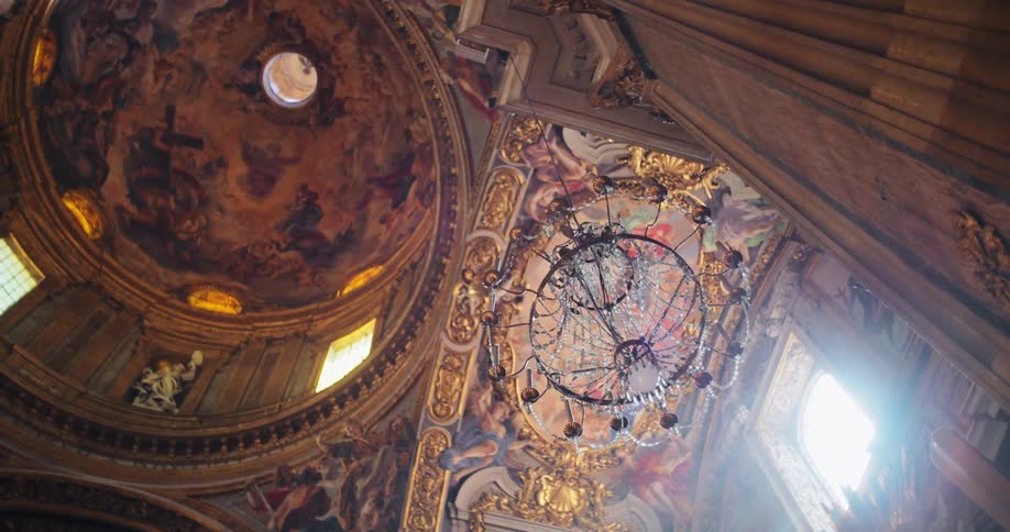 Church interior with colorful frescoes on the ceiling and a decorated dome illuminated by a central chandelier