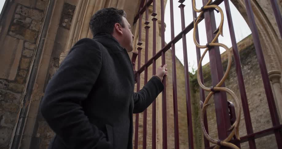 A man stares through a metal gate at an entrance in an ancient building during daytime
