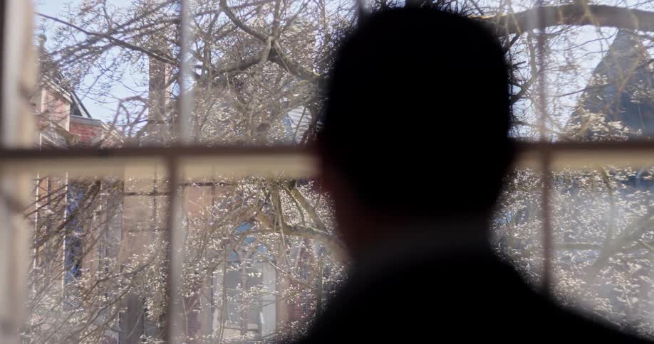 Close up of a man looking outdoors through a window while standing indoors during daytime