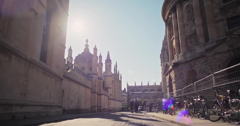 Church buildings with people walking down the streets and bikes parked on a railing fence beside the building at midday