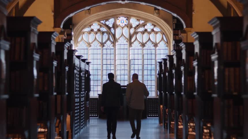 Two men walking down a library hallway