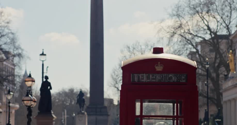 Statue on a tall column towers over a plaza while a vehicle drives past a red public phone booth on a cloudy winter day