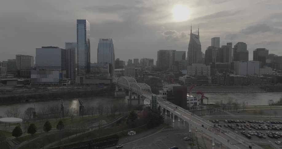 A city skyline view with a bridge over a river connecting two cities with the setting orange sunlight partially covered by clouds in the sky