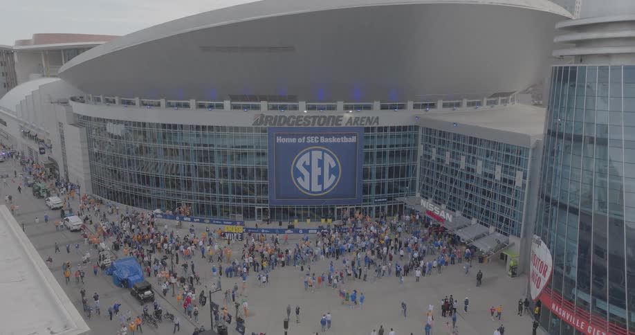 A massive crowd of sports fans is gathering outside the bridgestone arena which is hosting the sec basketball championship creating a bustling and energetic atmosphere