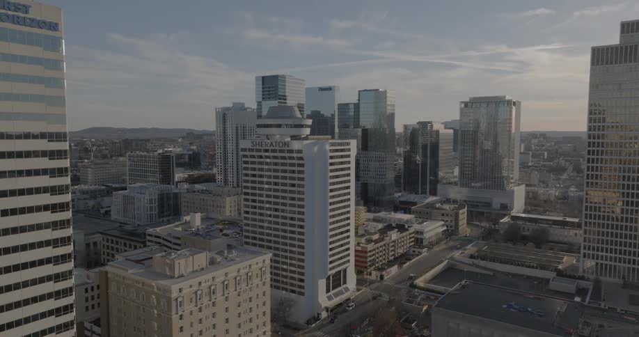 A large city skyline with numerous tall buildings and a flag flying from one of them slowly pans from right to left revealing a building with the word sheraton on its side