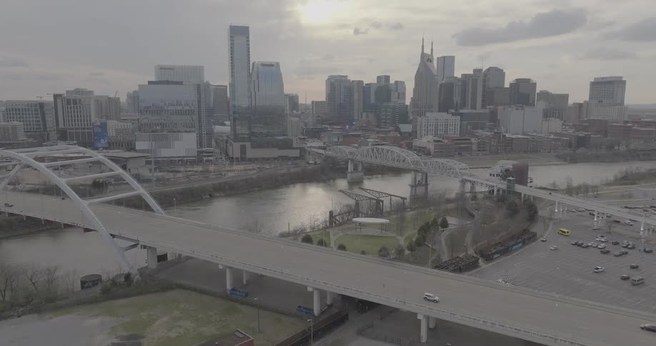 Traffic crosses the river on the two bridges bracketing a park located across from downtown on an overcast day