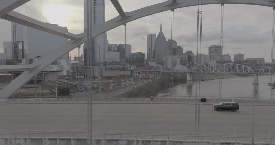Vehicles and pedestrians cross a bridge over a river near downtown on an overcast day