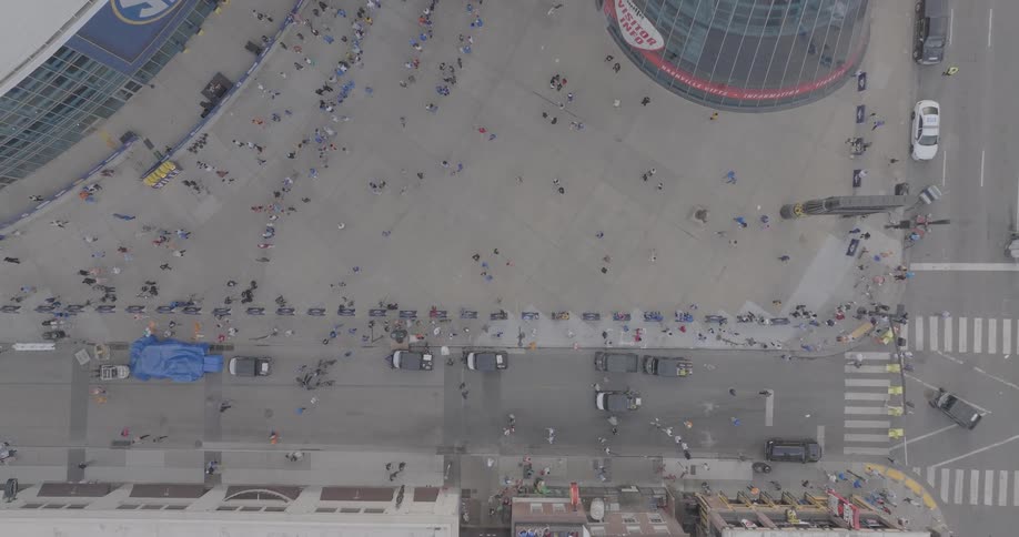 An aerial view of a crowd gathering outside an arena in downtown nashville during the day shows people lining up along barricades near several parked vehicles