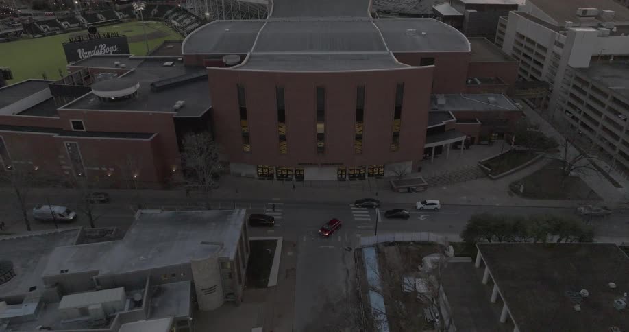 Vehicular and pedestrian traffic pass a building located next to a baseball stadium after dusk