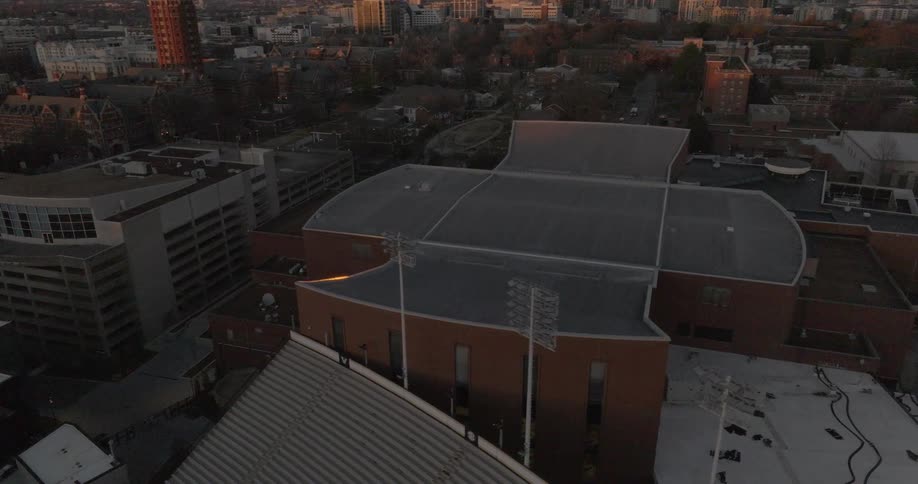 Aerial view of urban buildings at sunset highlighting a large structure with a curved gray roof