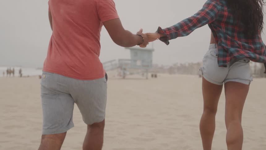 A man and a woman running hand in hand on the sandy beach