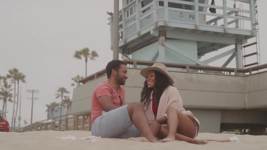 A man and a woman sitting on the beach sand talking