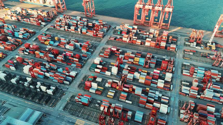 Aerial view of a port with red cranes and hundreds of containers arranged in rows near the sea