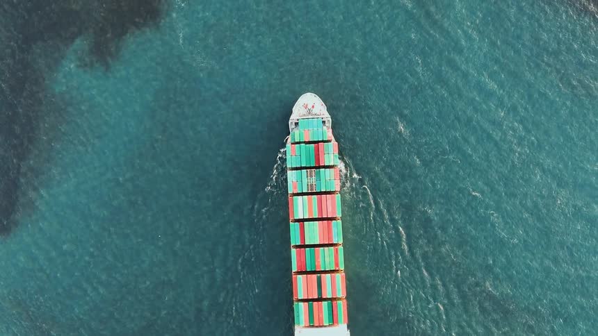 Cargo ship seen from above sailing in the sea with stacked colorful containers