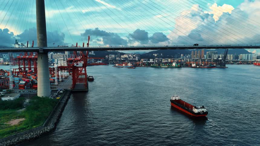 Port with cranes and containers under a cablestayed bridge with a cargo vessel sailing