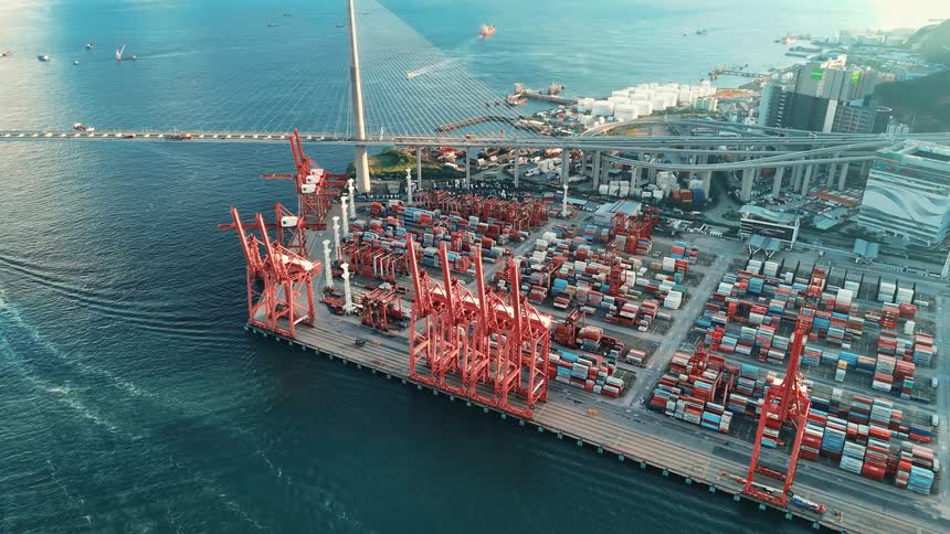 Port terminal with red cranes and containers next to a cablestayed bridge over the sea
