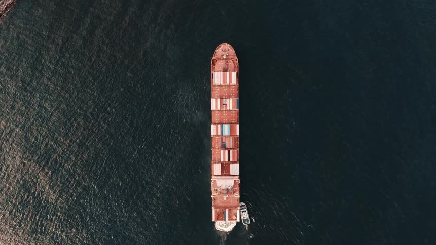 Aerial view of a container ship sailing in the sea with the assistance of a tugboat