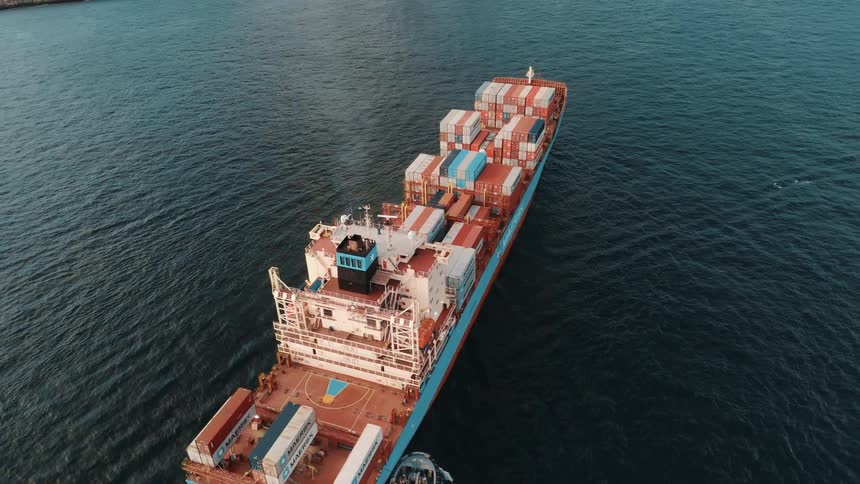 Aerial of a loaded cargo ship moving along the surface of a water body close to a city during daytime