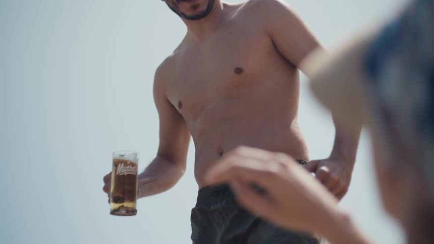 Shirtless man holding a glass of beer at the beach