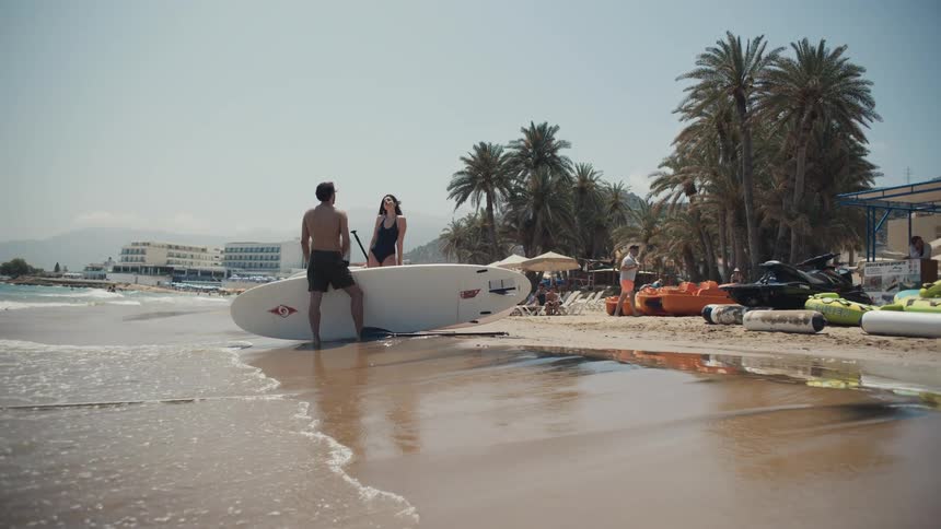 A man and woman lean on a surfboard and talk