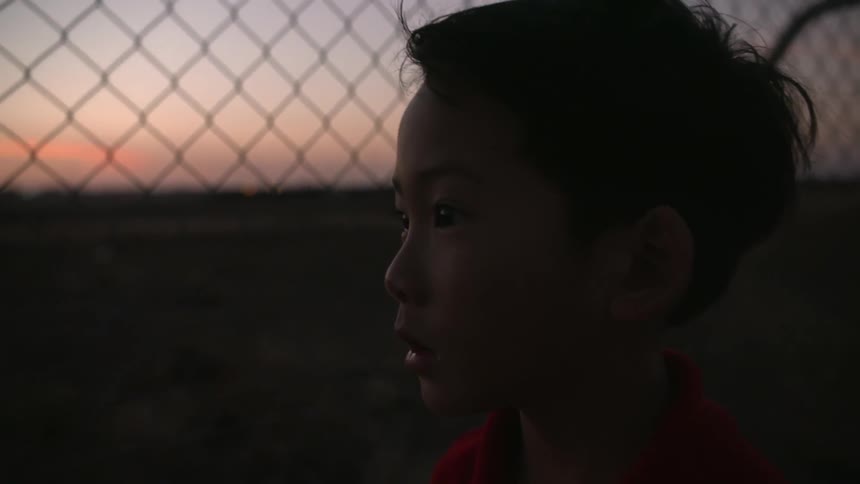 Boy in front of a chain link fence at sunset
