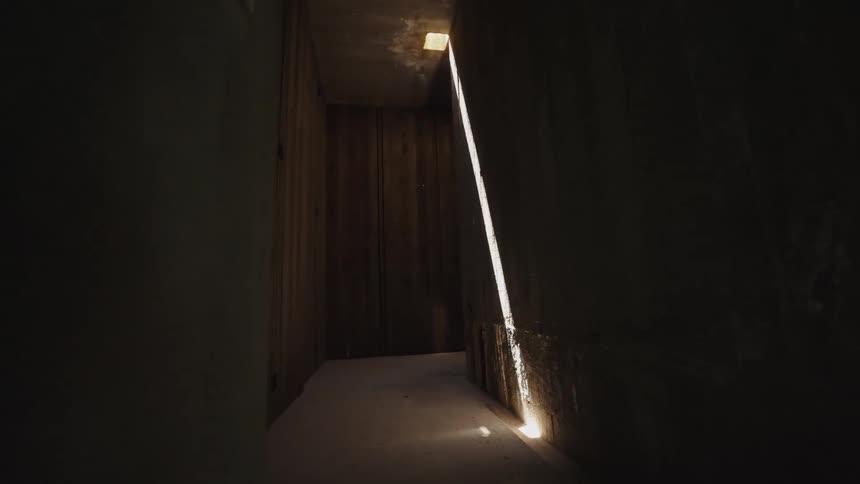 Beam of light enters through an opening illuminating the dark concrete wall