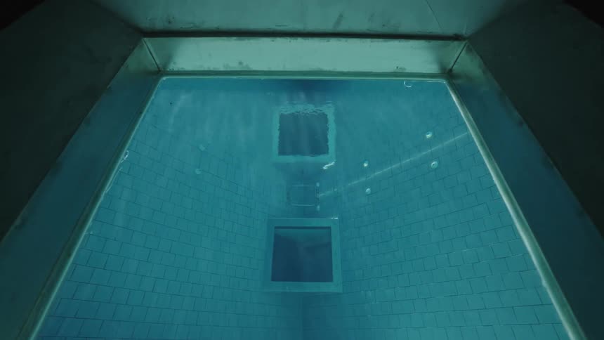 The video shows an underwater perspective of a swimming pool with a glassbottomed section ripples on the waters surface distort the view of the sky and the pools concrete edge