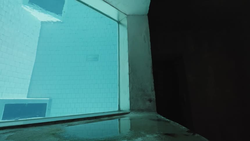 A unique perspective of a swimming pool is shown from an observation window with bright blue water and tiled walls visible inside the pool