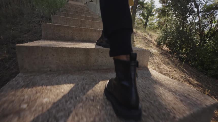 Black boots walk up stone steps in a wooded area